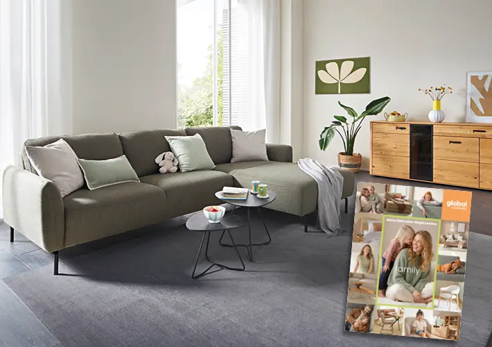 Graues Ecksofa mit Kissen, Couchtischen, Sideboard und Broschüre mit global wohnen family